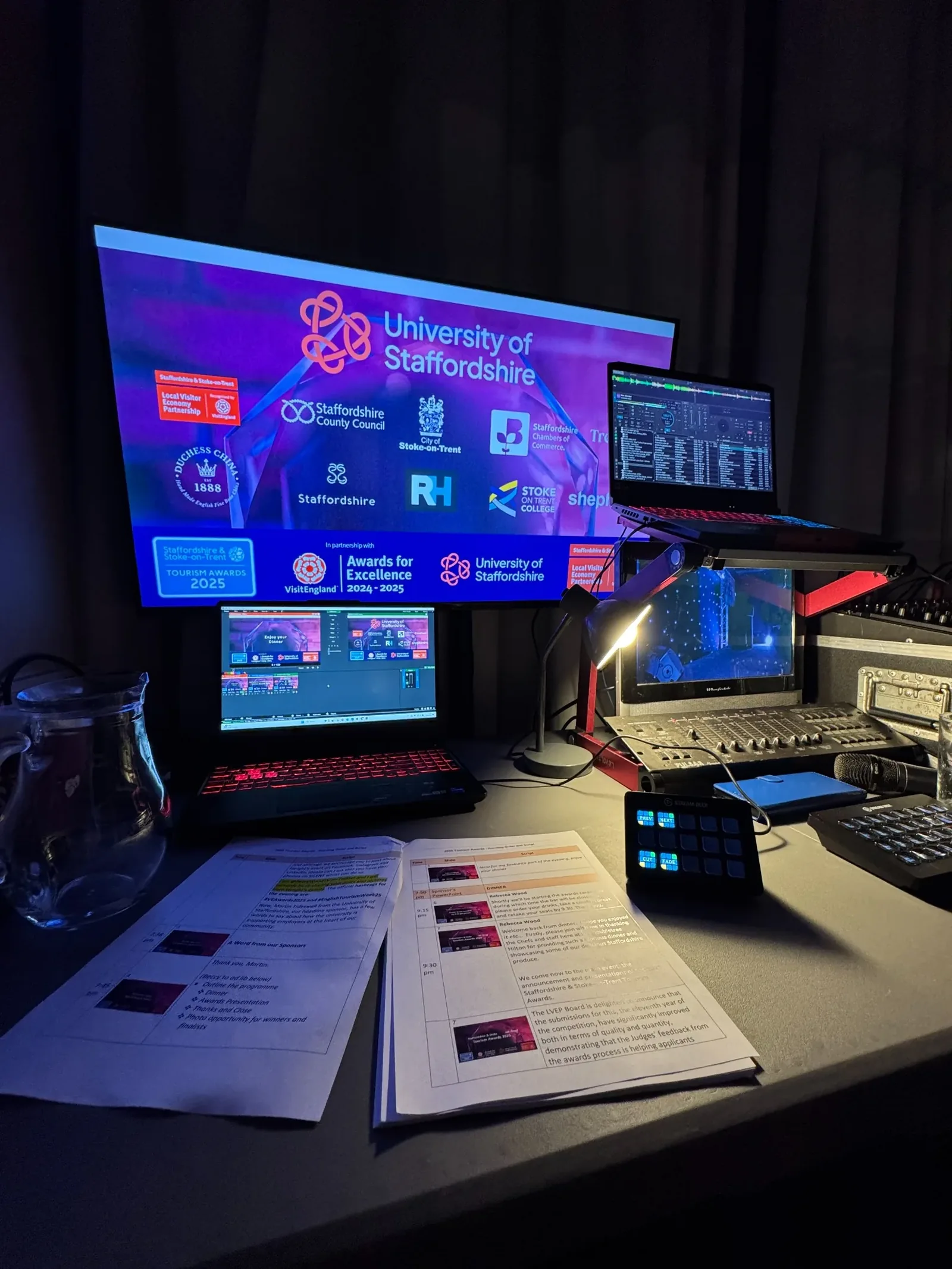 Production desk and screen controls beside an event stage